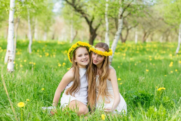 Girlfriends are sitting in the grass with wreaths of dandelions — Stock Photo, Image