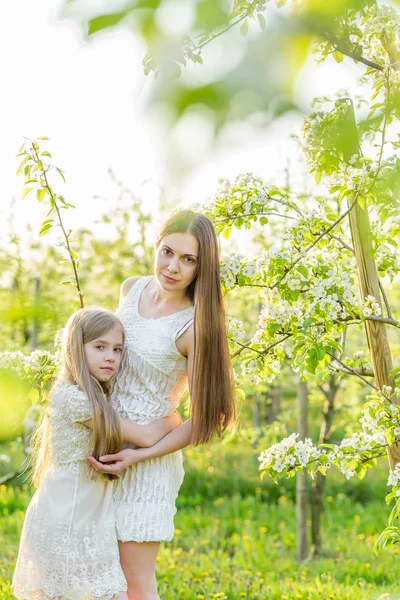 Beautiful mother and daughter in a blooming garden in the spring — Stock Photo, Image