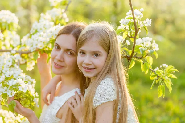 Beautiful mother and daughter in a blooming garden in the spring — Stock Photo, Image