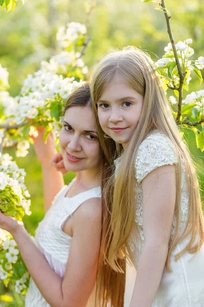 Beautiful mother and daughter in a blooming garden in the spring — Stock Photo, Image