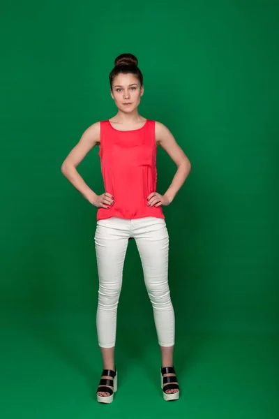 Όμορφη νεαρή κοπέλα σε μια κόκκινη μπλούζα και λευκό παντελόνι σε ένα gre — Φωτογραφία Αρχείου
