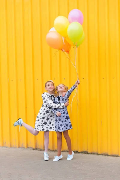Portrait of girls with balloons on yellow background — Stock Photo, Image