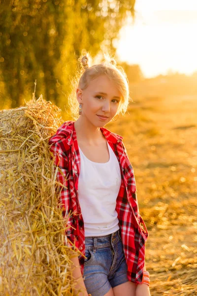 Jeune fille sur des gerbes de paille dans un champ — Photo