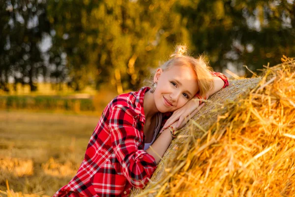 Young girl on straw sheaves in a field — Stock Photo, Image
