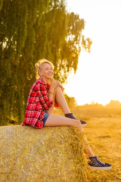 Young girl on straw sheaves in a field — Stock Photo, Image