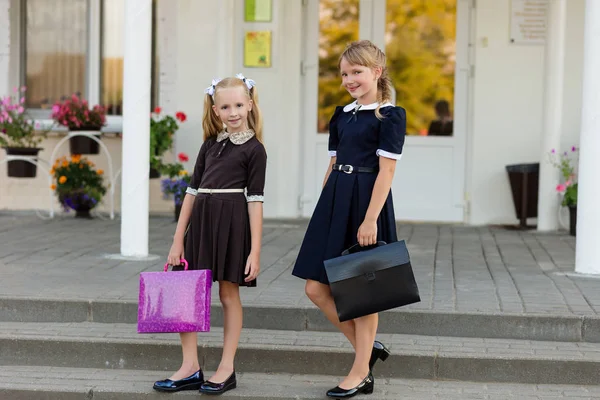 Zwei Mädchen in Schuluniform mit Aktentaschen stehen auf der — Stockfoto