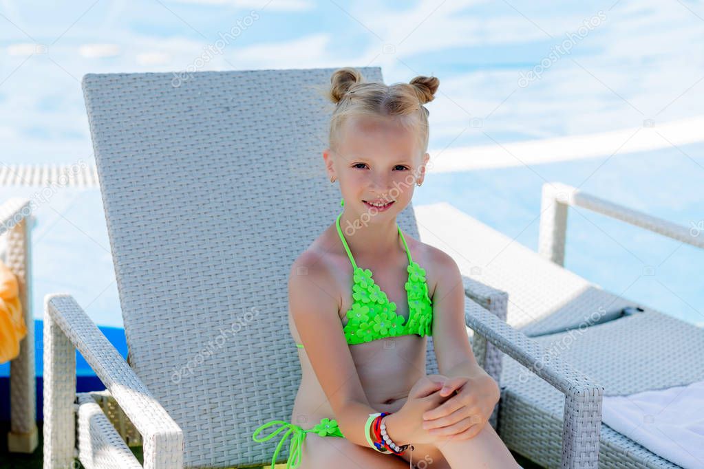 Young girl in a swimsuit on a shelf by the pool