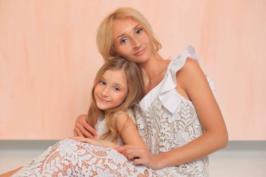 Mom with her daughter in white dresses in the studio.
