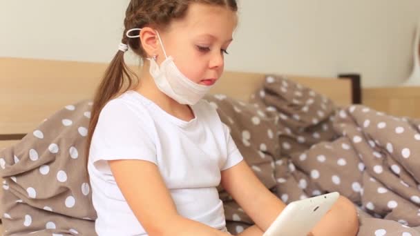 Маленькая девочка в респираторной маске сидит в карантине на планшете — стоковое видео