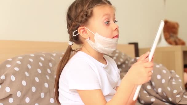 Κοριτσάκι με αναπνευστική μάσκα κάθεται σε καραντίνα σε δισκίο — Αρχείο Βίντεο