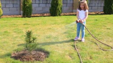 Elinde hortumla yeşil çimenleri sulayan küçük bir kız.