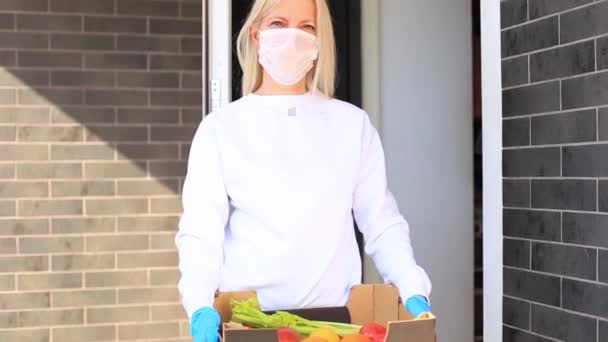 Жінка стоїть у дверному отворі з коробкою з маскою — стокове відео