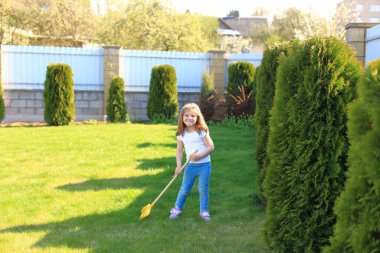 Küçük kız evin yakınındaki çimlere bakmasına yardım ediyor.