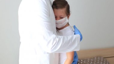 Doktor, solunum maskesi takmış küçük bir kıza sarılıyor..