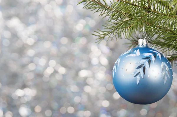 Blaue Weihnachtskugel auf einem Weihnachtsbaumzweig über verschwommenem, glänzendem Hintergrund, Nahaufnahme. — Stockfoto
