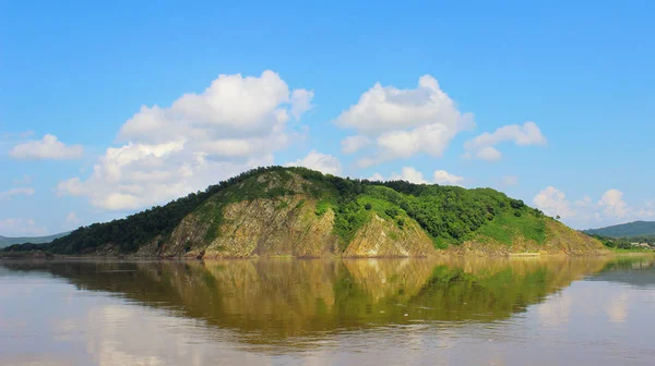 Isola rocciosa solitaria in acqua calma con riflesso pulito e cielo blu. Alberi verdi sulla cima dell'isola rocciosa. Vista dall'acqua a terra . — Foto Stock
