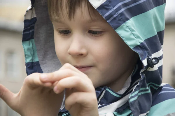 Jongetje nieuwsgierig van zijn hand. Jongen in stripe kap glimlachen — Stockfoto