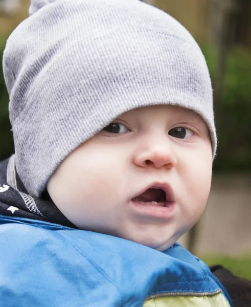 Babyjongen opent mond met twee tanden. Kleine jongen in een grijze kap. Baby als misdaad bandit — Stockfoto