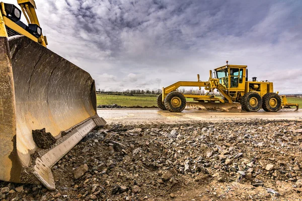 道路の建設中の土地をレベルアップし 滑らかにするための掘削機 — ストック写真