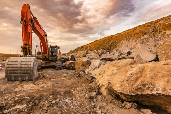 Kazıcı, bir yol inşaatında toprak ve taşı hareket ettiriyor.