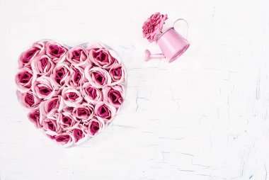 Kırık beyaz bir arka plan üzerinde kalp şeklinde yapay pembe güller. 