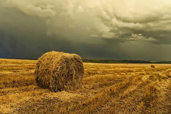 En runda höstack på ett clearade krokiga fält och en stormig himmel. — Stockfoto
