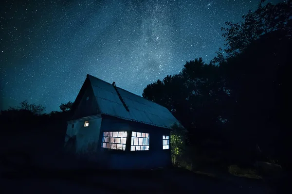 Basit bir kırsal çiftlik evi ve yıldızlı gökyüzünün yukarıda gece fotoğrafı.