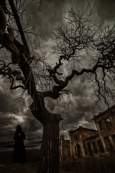 一个女人在一个帽衫和可怕的废墟背景下的树枝的黑色剪影. — 图库照片