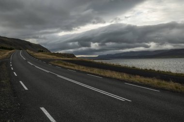 Issız bir asfalt yol tepelere doğru gidiyor. İzlanda. Seyahat ve macera ruhu.