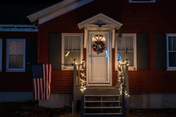 Gece fotoğraf küçük bir basit ev sundurma Noel çelenk ve çelenk ile dekore edilmiştir. Amerika'nın bayrak rüzgarda geliştirmektedir. Noel masalı. Amerika Birleşik Devletleri. Maine