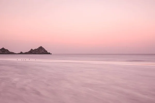 A beautiful sunset on the deserted shore of the Indian Ocean.  Idylistic minimalistic artistic photo of the sea at sunset. Calm of the sea evening, long exposure, frozen water.