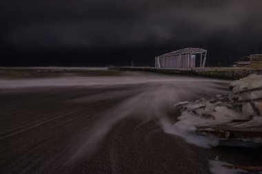 Gece fotoğraf şiddetli kış deniz. Uzun pozlama. Dalgalar kıyıya geliyor, iskele ve deniz köpüğü suda merdiveni.