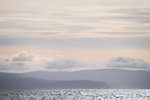 A gentle view of the ocean line and the silhouettes of the mountains in the haze in soft light. Lines of landscape minimalism, simplicity of nature lines. ICELAND