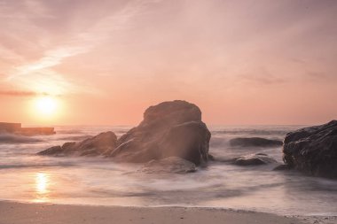 Sahilde güzel bir pembe şafak. Kırma taş karşı dalgalar. Uzun pozlama