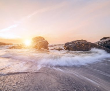 Sahilde güzel bir şafak. Dalganın kıyıya yaklaşıyor. Kırma taş karşı dalgalar. Uzun pozlama