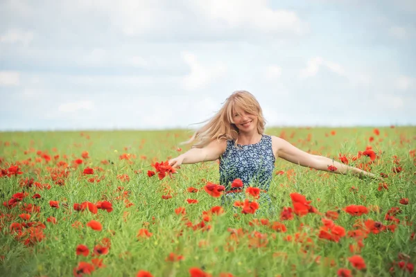 a natural woman with blond hair whirls in a field with beautiful red poppies. An atmosphere of carefree joy of happiness.