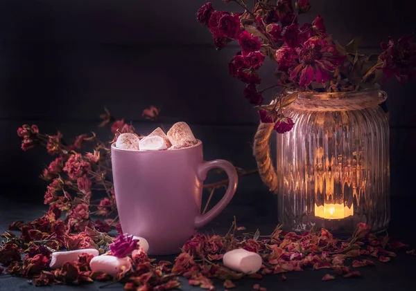 Dark still life. Cup with cocoa and marshmallows and small flowers of roses on a dark background. Cozy autumn winter mood