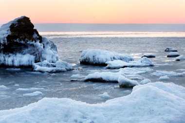 Deniz kıyısında dondurucu kış şafağı. Kıyı ve taşlar kar ve buzla kaplı..