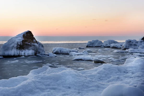 Frosty winter dawn on the seashore. The shore and stones covered with snow and ice.