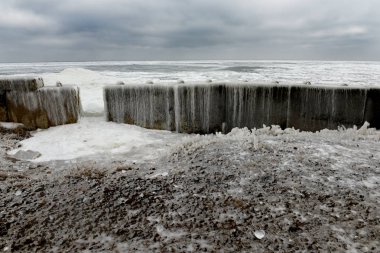 Donmuş suyla kasvetli, dramatik kış denizi. Karada buz ve karla kaplı beton yapılar..