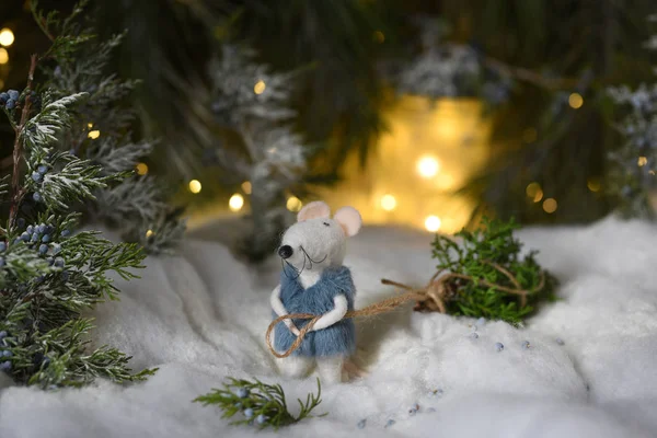 A toy white mouse a rat in a fur coat drags a Christmas tree from a forest among sparkling magic lights by a rope. Symbol of 2020. Fairy-tale magic festive decoration