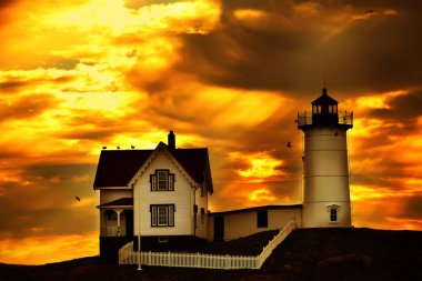 Deniz feneri ve tepedeki fenerin bekçisinin evi gün batımına karşı. Atlantik Okyanusu kıyıları ve adadaki deniz fenerinin dramatik fantastik fotoğrafı. Atlantik Okyanusu. Usa. Maine. Nubble York 
