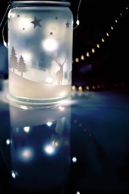 Işıklı parlak bir fener ve siyah arka planda çelenklerin renkli bokeh 'i. Noel süslemeleri ve ruh hali. Işık saçan koyu renkli bir fotoğraf..