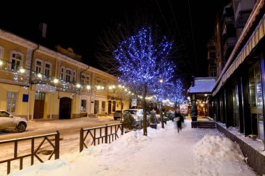 Yılbaşı ve yeni yıl tatili boyunca parlak çelenkler ve süslemelerle süslenmiş karlı bir caddenin gece fotoğrafı. Kış festivali sokak manzarası. Odessa 'da. Ukrayna.