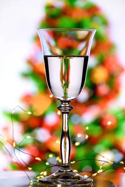 A glass of champagne with sparkling wine and a blurred image of a Christmas tree on a white background with reflection of a Christmas tree in a glass. New Year and Christmas celebration.