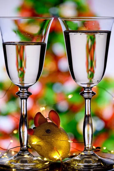 Two glasses with sparkling wine and a sparkling golden rat against a blurred image of a Christmas tree.