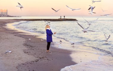 The girl walks on a deserted beach in the winter and feeds the seagulls.