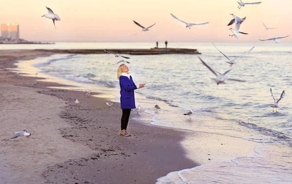 The girl walks on a deserted beach in the winter and feeds the seagulls.