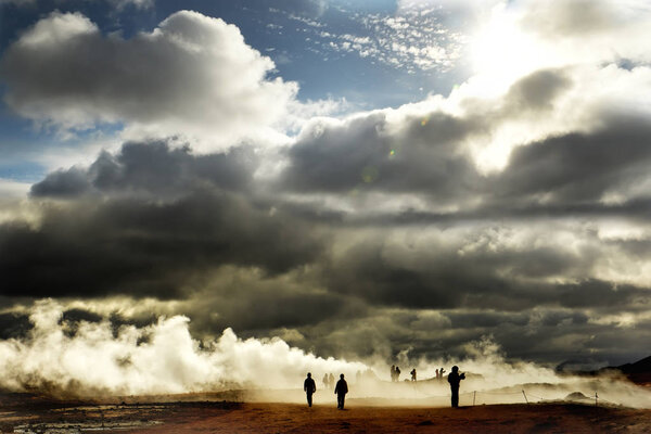 Valley with geothermal springs and geysers. Silhouettes of tourists wandering among clubs a couple erupting from the ground. Geothermal zones a Naumafjal Hverir in the north-eastern part of Iceland.