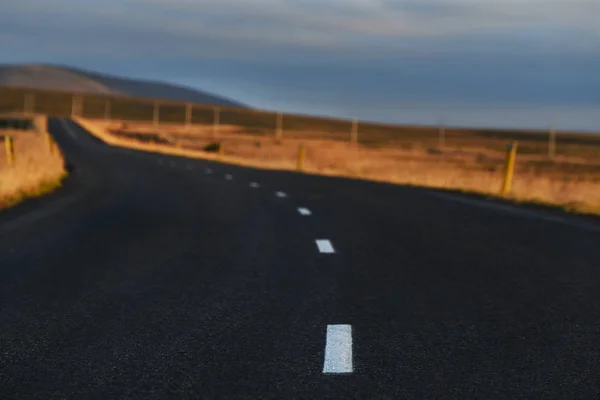 a deserted asphalt road running away into the hills. Iceland. The spirit of travel and adventure. Very soft selective focus in the foreground.